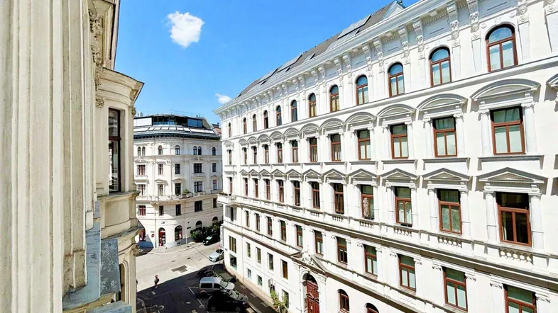 Historische Gebäude mit klassischer Architektur und Blick auf die belebte Straße unter blauem Himmel.