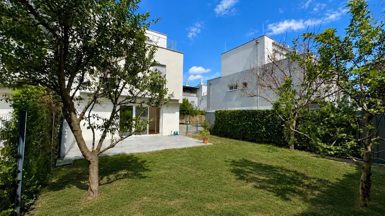 Gepflegter Gartenbereich mit Rasenfläche und kleiner Terrasse hinter einem modernen Wohnhaus.