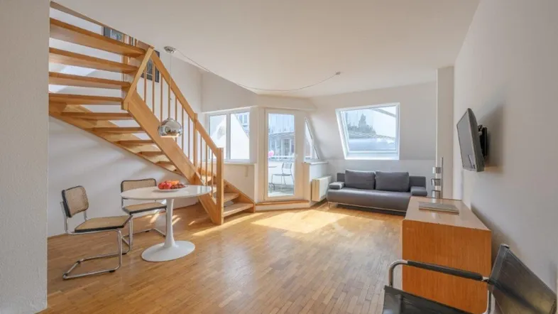Helles Wohnzimmer mit Holztreppe, Parkettboden und Zugang zum Balkon.