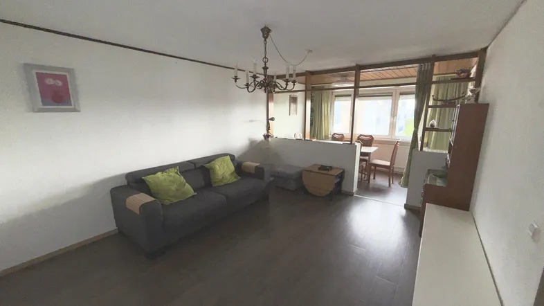 Gemütlicher Wohnbereich mit Sofa, Kronleuchter und Übergang zum Essbereich, ausgestattet mit dunklem Laminatboden.