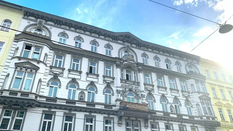 Historisches Gebäude mit reich verzierter Fassade, vielen Fenstern und dem Schriftzug "AUGARTEN-HOF".