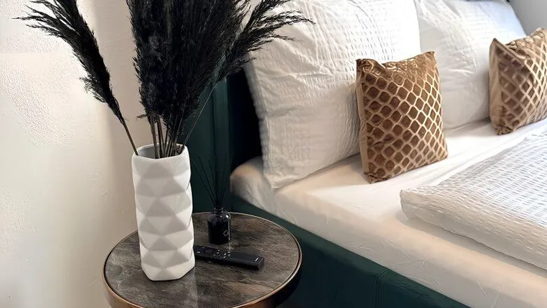 Gemütliches Schlafzimmer mit modernem grünen Bett, stilvollem Nachttisch und dekorativer Pampasgras-Vase.