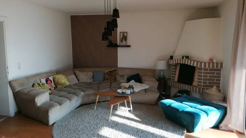Gemütliches Wohnzimmer mit großem Ecksofa, Kamin und Holzboden, hell durchflutet.