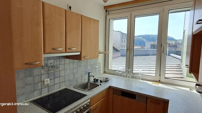 Funktionale Einbauküche mit Holzschränken, Fliesenrückwand und großem Fenster mit Dachblick.