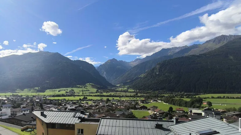 Panoramablick über ein malerisches Tal mit Bergen, grünen Feldern und einer charmanten Ortschaft.