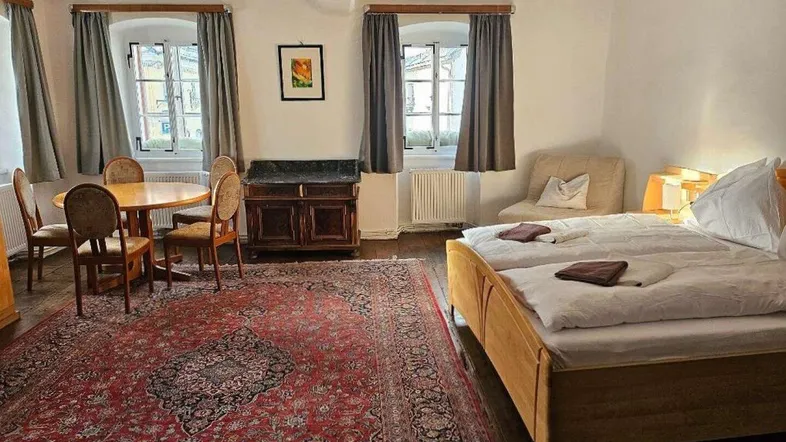 Gemütliches Schlafzimmer mit traditionellem Teppich, zwei Fenstern und einem kleinen Essbereich.