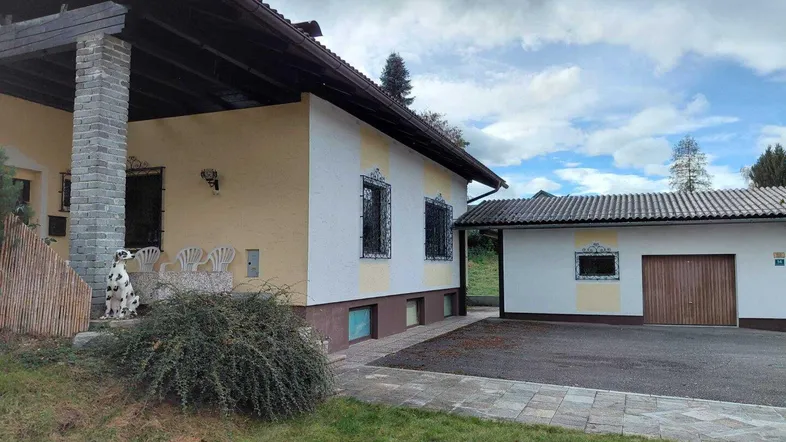 Hausfassade mit angrenzender Garage und gepflegtem Vorgarten unter bewölktem Himmel.