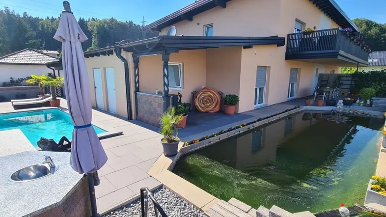 Großzügige Terrasse mit Swimmingpool, Naturteich und Blick auf die umliegende Landschaft.