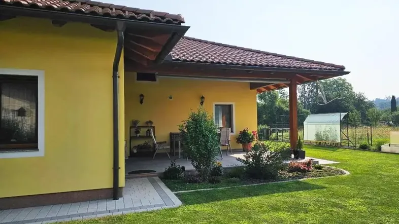 Überdachte Terrasse mit Garten und gepflegter Rasenfläche am gelben Haus.