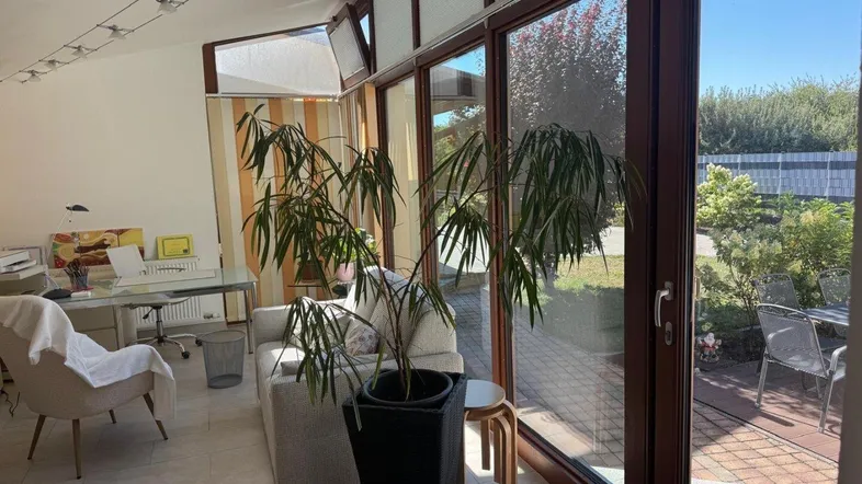 Heller Wintergarten mit großen Fenstern, der als Büro- und Wohnbereich genutzt wird und Blick ins Grüne bietet.