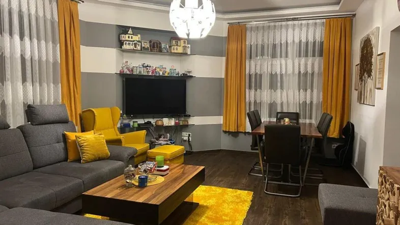 Geräumiger Wohn-Essbereich mit modernem Design, dunklem Laminatboden und gelben Akzenten.