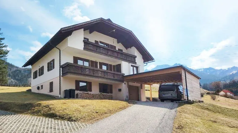 Traditionelles Chalet in den Bergen mit Holzbalkonen, Carport und weitem Blick auf die Landschaft.