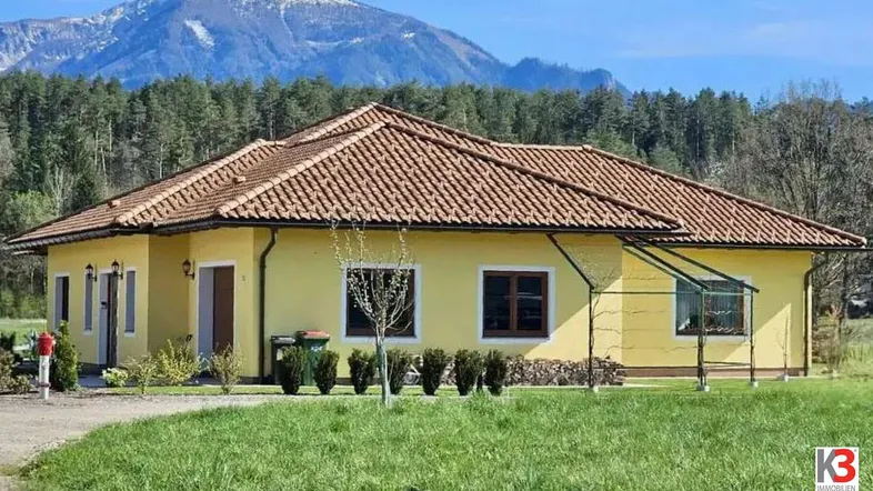 Einfamilienhaus mit gelber Fassade und Ziegeldach in ländlicher Umgebung mit Bergblick.