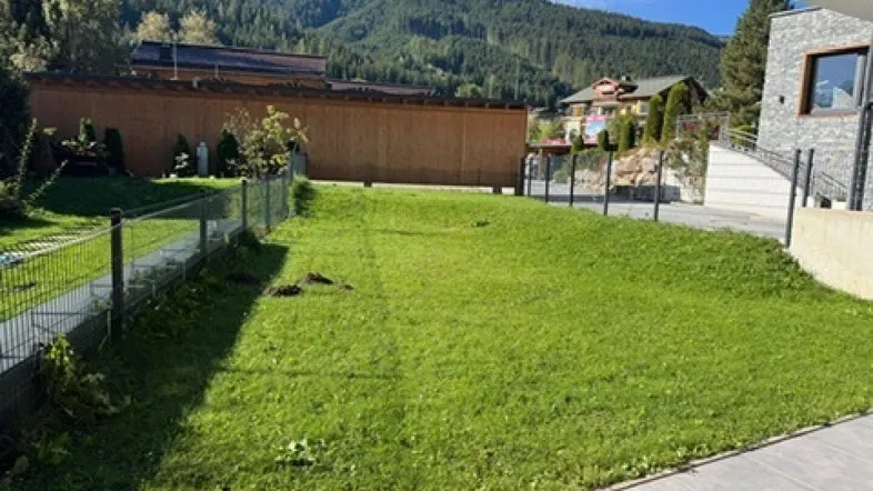 Grüne Rasenfläche mit Bergblick und umliegenden Gebäuden unter blauem Himmel.