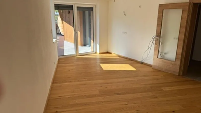 Helles Zimmer mit neuem Parkettboden und Zugang zu einem Außenbereich, ideal für Wohnzwecke.