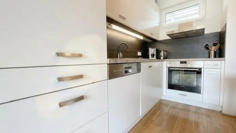 Moderne Einbauküche mit weißen Fronten, integriertem Geschirrspüler, Ofen und Holzfußboden.