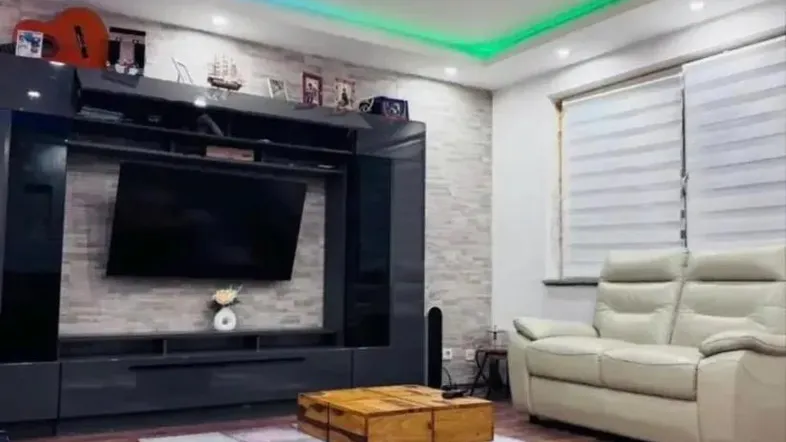 Modernes Wohnzimmer mit farbiger LED-Beleuchtung, großem TV-Möbel und Holzboden.