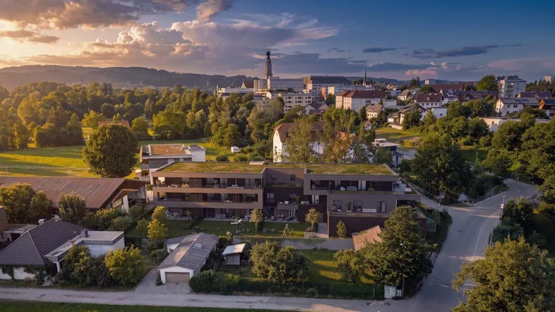 Luftaufnahme eines modernen Wohnkomplexes mit Gründächern in ländlicher Umgebung bei Sonnenuntergang.