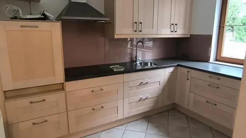 Helle Einbauküche mit hellen Holzfronten, dunkler Arbeitsplatte und Fliesenboden.