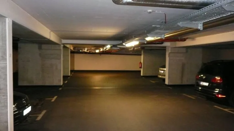 Geräumige Tiefgarage mit markierten Stellplätzen und sichtbaren Installationen an der Decke.