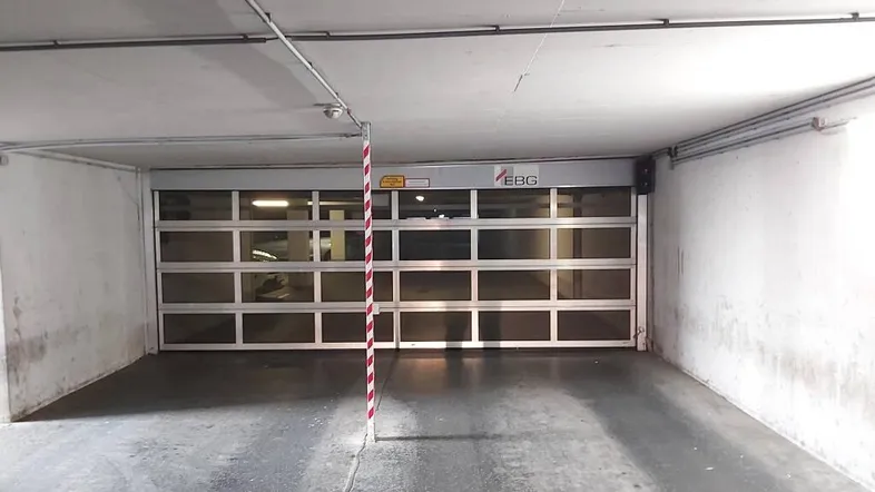 Saubere und gut beleuchtete Tiefgarageneinfahrt mit automatischem Rolltor und Betonboden.