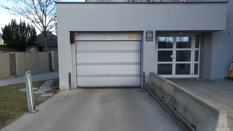 Eingang zu einer Tiefgarage mit Rolltor und Rampe, neben dem Haupteingang des Gebäudes.
