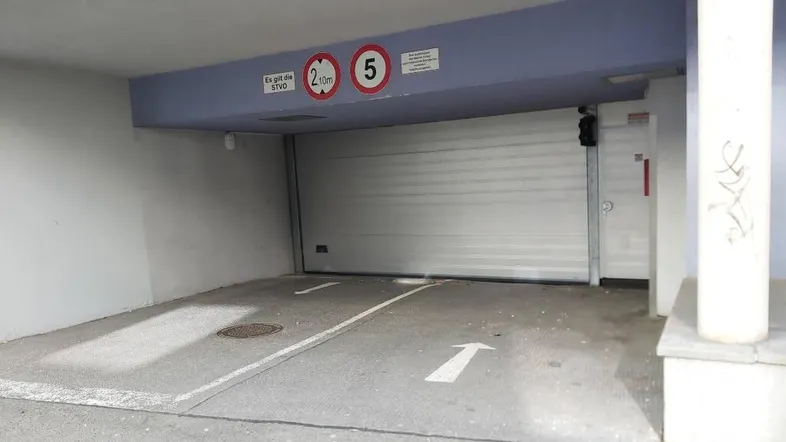 Einfahrt zur Tiefgarage mit Höhenbegrenzung und Rolltor.