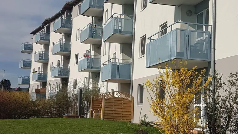 Moderne Fassade eines Mehrfamilienhauses mit zahlreichen Balkonen und angrenzender Grünfläche.