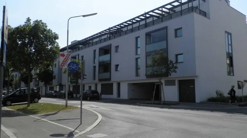 Modernes Apartmentgebäude mit weißer Fassade, großen Fenstern und Dachterrasse entlang einer Straße.