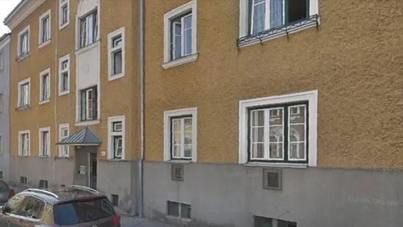 Fassade eines Mehrfamilienhauses mit gelb-braunem Putz und weißen Fenstern an einem sonnigen Tag.
