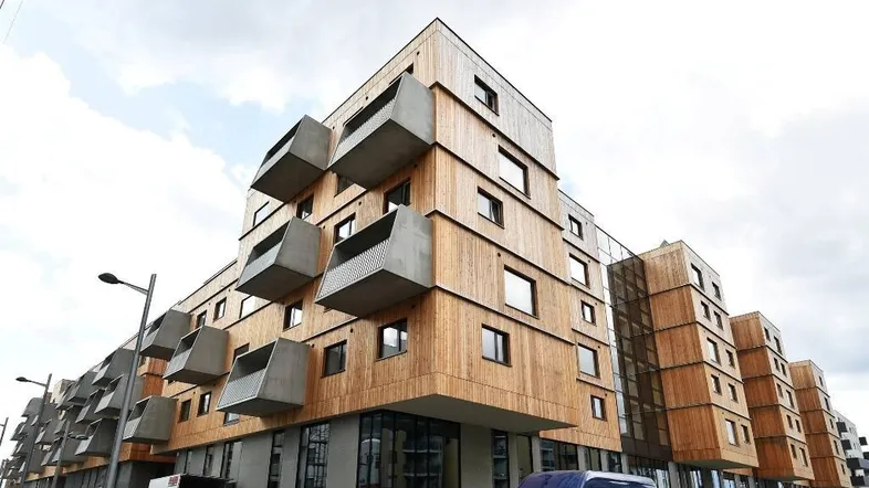 Modernes Gebäude mit Holzfassade und markanten Betonbalkonen unter bewölktem Himmel.