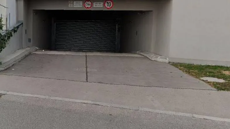 Einfahrt zu einer Tiefgarage mit Rampe und geschlossenem Rolltor in einem modernen Gebäude.