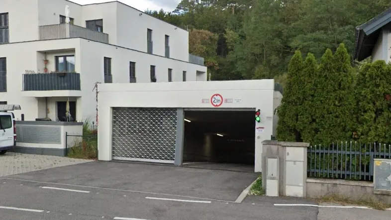 Einfahrt zur Tiefgarage eines modernen Wohngebäudes mit Schranke und Höhenbegrenzung.