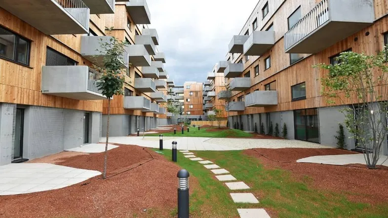 Moderner Innenhof zwischen Wohngebäuden mit Holzfassaden und Betonbalkonen, gestaltet mit Rasenflächen und Trittsteinen.