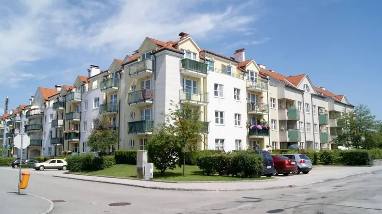 Modernes Mehrfamilienhaus mit vielen Balkonen und gepflegter Außenanlage unter blauem Himmel.