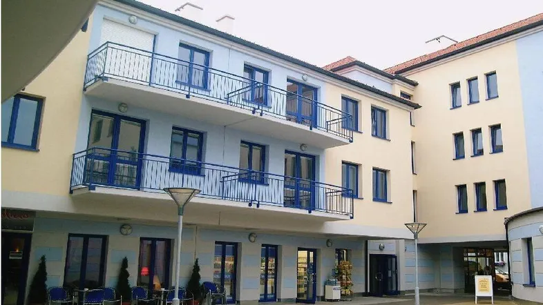 Moderner Gebäudekomplex mit hellblauer und beiger Fassade, Balkonen und einem belebten Innenhof.