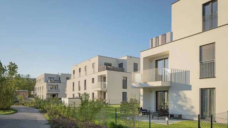 Reihe moderner weißer Wohngebäude mit Balkonen und kleinen Terrassen unter blauem Himmel.