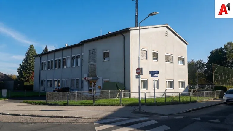 Außenansicht eines schlichten, gut erhaltenen Bürogebäudes mit mehreren Fenstern und einem grünen Umfeld unter blauem Himmel.
