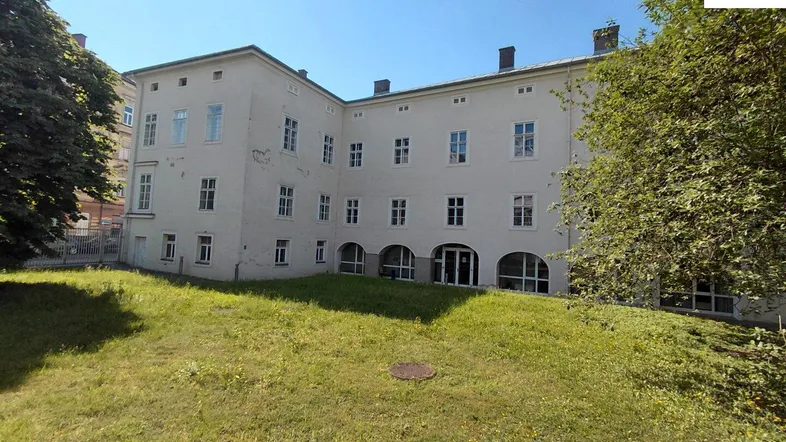 Gebäudeansicht von außen mit einer großen Rasenfläche im Vordergrund und vielen Fenstern.