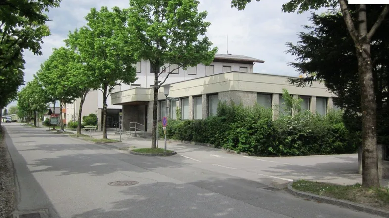 Gebäudeansicht von der Straße mit Bäumen und einem Gehweg, der zum Eingang führt.