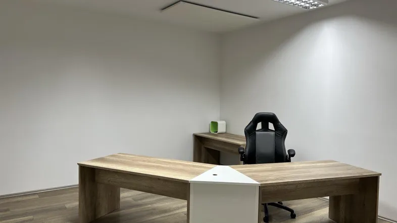 Modernes Büro mit L-förmigem Schreibtisch und ergonomischem Stuhl in einem hellen Raum.