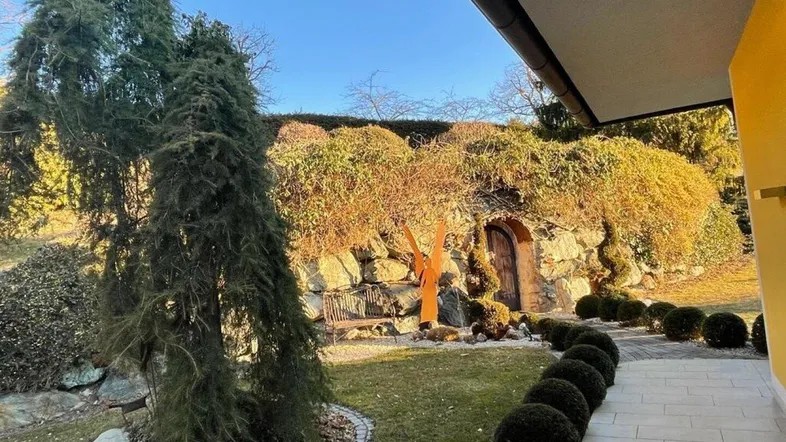Sonnige Gartengestaltung mit Felsen, einem kleinen Höhleneingang und einem gepflasterten Weg.