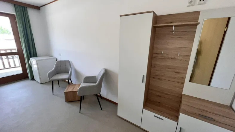 Heller Raum mit modernem Kleiderschrank, zwei bequemen Sesseln und Zugang zu einem Balkon.