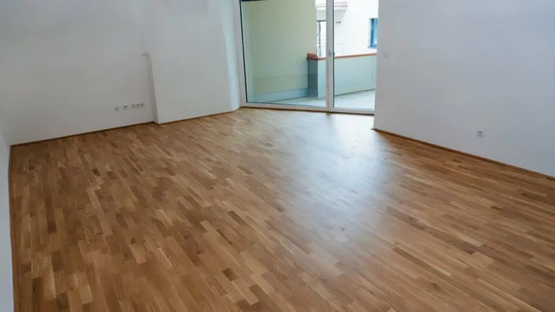 Geräumiges Zimmer mit Holzparkett und Zugang zu einem Balkon.