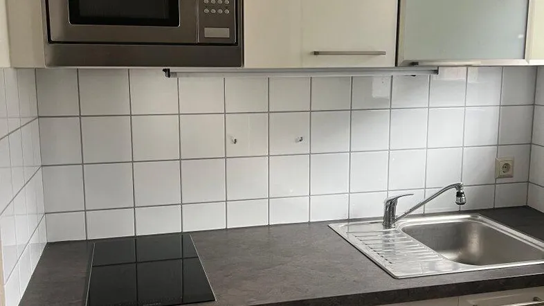 Kompakte Küche mit weißen Schränken, dunkler Arbeitsplatte, integrierter Mikrowelle und Induktionskochfeld.