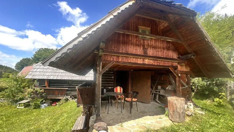 Eine rustikale Holzhütte mit überdachtem Eingangsbereich und kleiner Sitzgelegenheit im Freien.