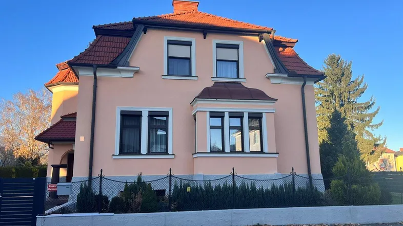 Helles Einfamilienhaus mit rosa Fassade, Mansarddach und traditionellen Fenstern unter blauem Himmel.