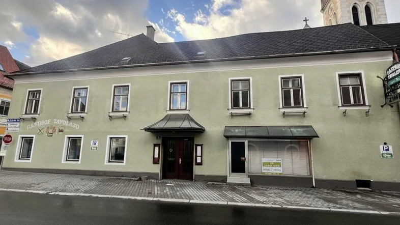 Vorderansicht des Gasthofs mit traditioneller Fassade und Blick auf die Kirche im Hintergrund.
