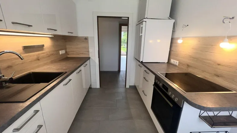 Moderne Küche mit weißen Schränken, Holzakzenten, Induktionskochfeld und Fliesenboden.