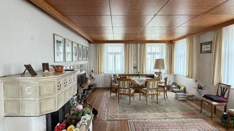 Geräumiges Wohnzimmer mit Holzboden, Holzbalkendecke und einem traditionellen Kachelofen.